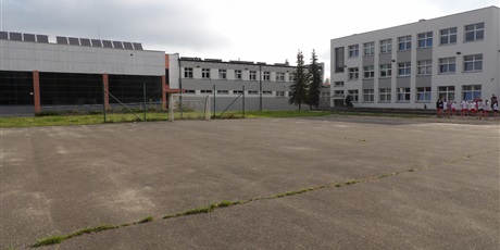 Powiększ grafikę: Zdjęcie szkoły od strony boiska wraz z jego fragmentem. Na zdjęciu znajdują się uczniowie podczas lekcji W-F'u.